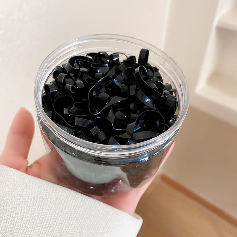 Hand holding clear container filled with small black plastic hair ties or elastics in a minimalist style
