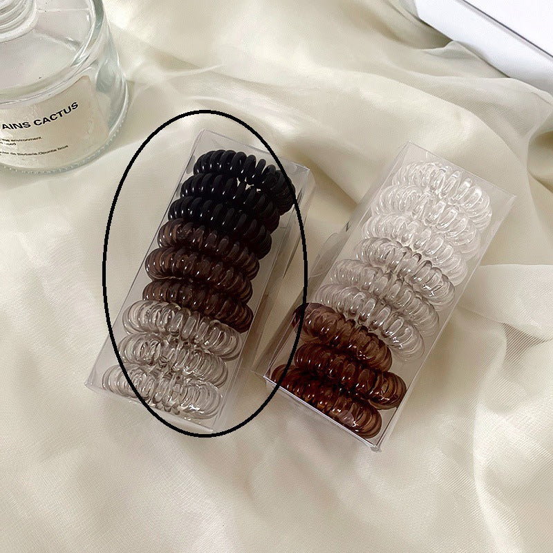 Two clear packages of spiral hair coils in various shades including black, brown and clear, displayed on white fabric