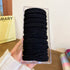 Hand holding clear plastic package of black elastic hair bands stacked neatly, approximately 20 pieces visible