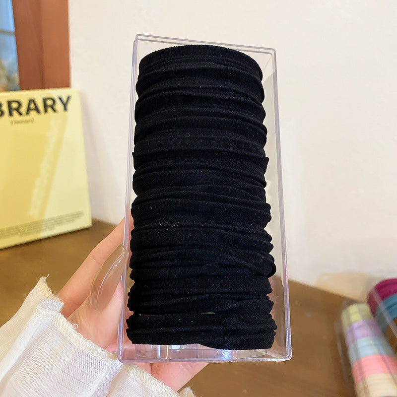 Hand holding clear plastic package of black elastic hair bands stacked neatly, approximately 20 pieces visible