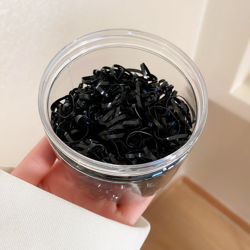 Hand holding clear plastic container filled with small black elastic hair ties, showing glossy texture and tangled arrangement