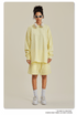 Woman in pale yellow sweatshirt and shorts set with sunglasses, headphones and white sneakers