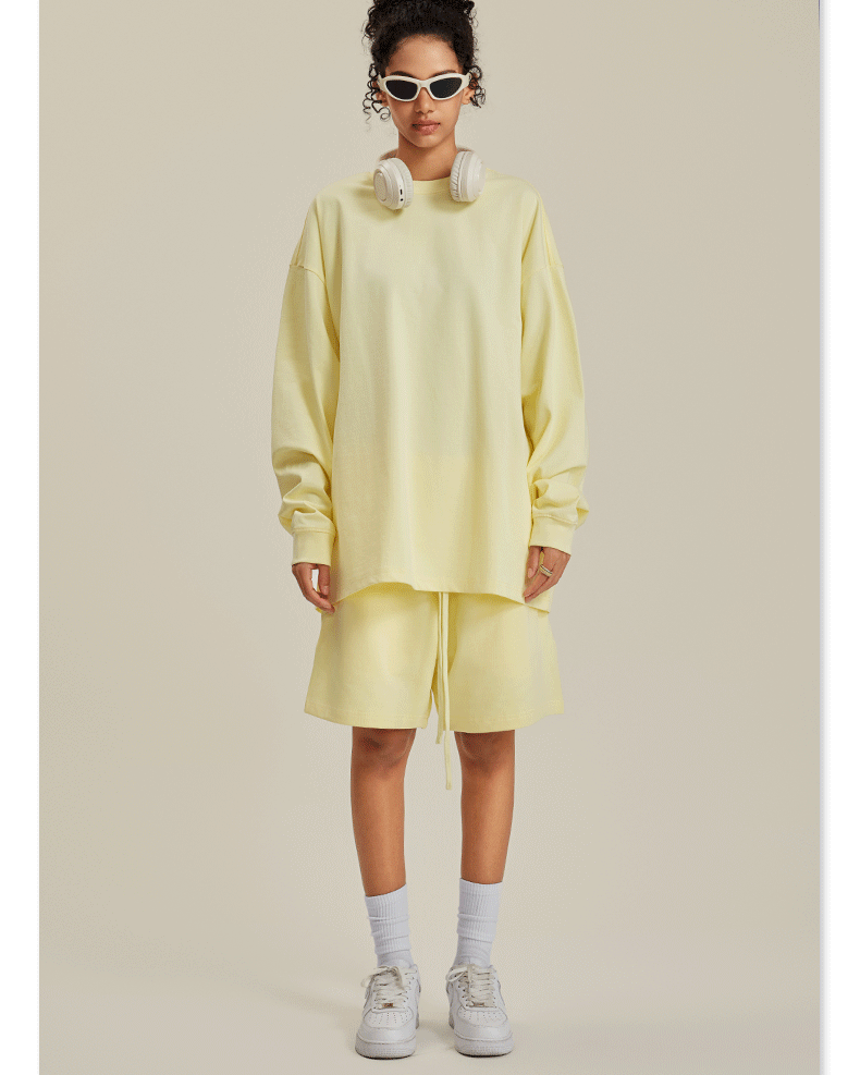 Woman in pale yellow sweatshirt and shorts set with sunglasses, headphones and white sneakers