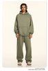 Model wearing olive green hoodie and sweatpants set with silver headphones against cream background
