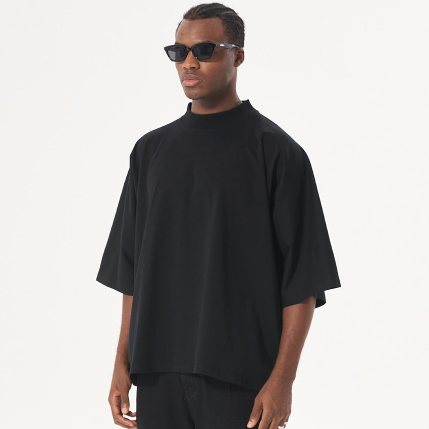A model wearing black sunglasses and an oversized black mock neck t-shirt with dropped shoulders against a white backdrop