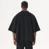 Back view of model with braided hair wearing black oversized t-shirt with mock neck collar and black cargo pants