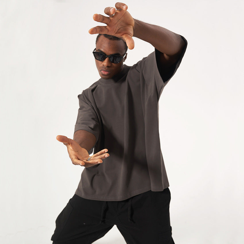 Model in black sunglasses making framing gesture wearing charcoal mock neck t-shirt and black pants against white background