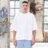 Model wearing white oversized t-shirt and light blue jeans standing in industrial setting with weathered walls and windows