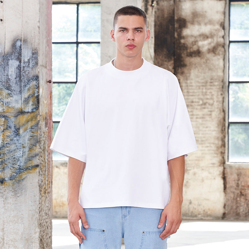 Model wearing white oversized t-shirt and light blue jeans standing in industrial setting with weathered walls and windows