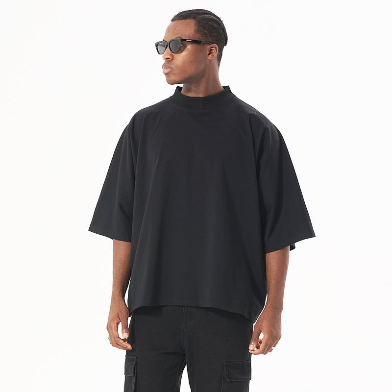 Side profile of model in black sunglasses wearing oversized black mock neck t-shirt and black cargo pants against white background
