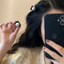 Mirror selfie showing black hair clips with pearl accents in use, holding iPhone 12 for photo