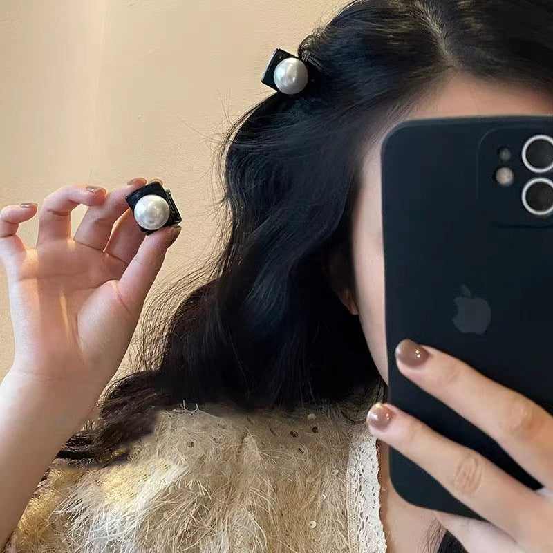 Mirror selfie showing black hair clips with pearl accents in use, holding iPhone 12 for photo