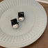 Two black mini hair clips with white pearls displayed on decorative white plate