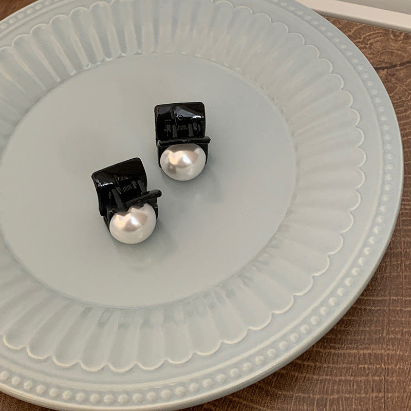 Two black mini hair clips with white pearls displayed on decorative white plate