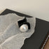 Close-up of black mini hair clip with pearl detail on tissue paper and black packaging