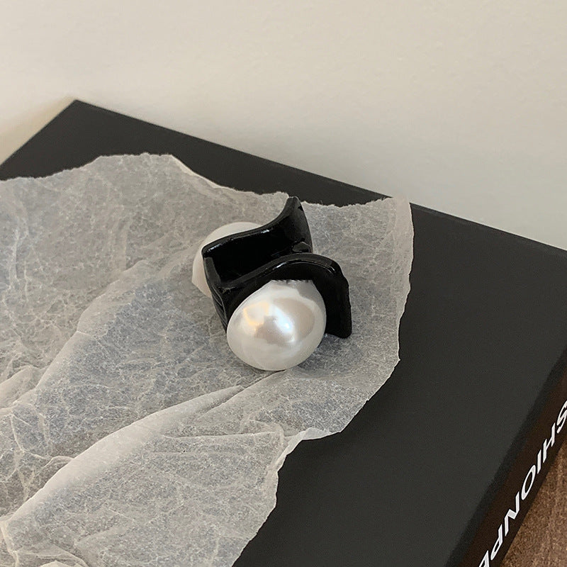 Close-up of black mini hair clip with pearl detail on tissue paper and black packaging