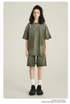 Model with curly hair wearing olive green t-shirt and matching shorts with white socks and black sneakers against cream background