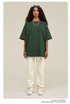 Woman wearing oversized dark green t-shirt with cream sweatpants, white sneakers and beaded necklace against neutral backdrop