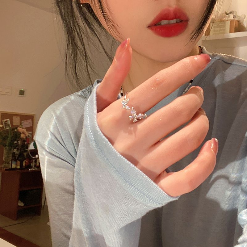Woman showing off a silver butterfly ring while wearing a soft blue sweater, with red lips in focus