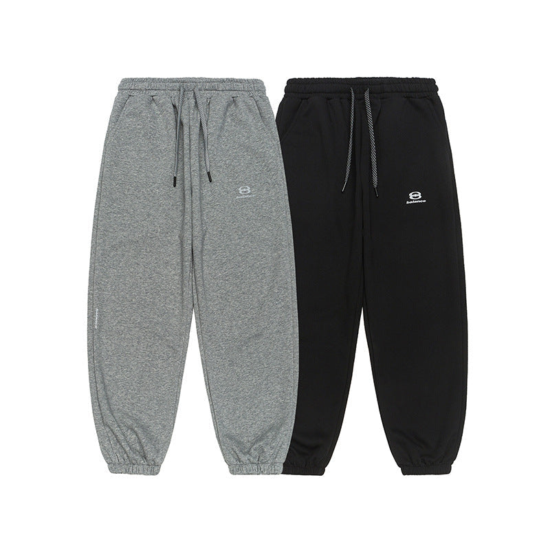 A pair of gray and black jogger sweatpants with elastic cuffs, drawstring waistbands, and small embroidered logos