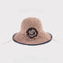  A pink woven sun hat with a navy crochet flower detail, featuring a flexible brim and an intricate woven texture.