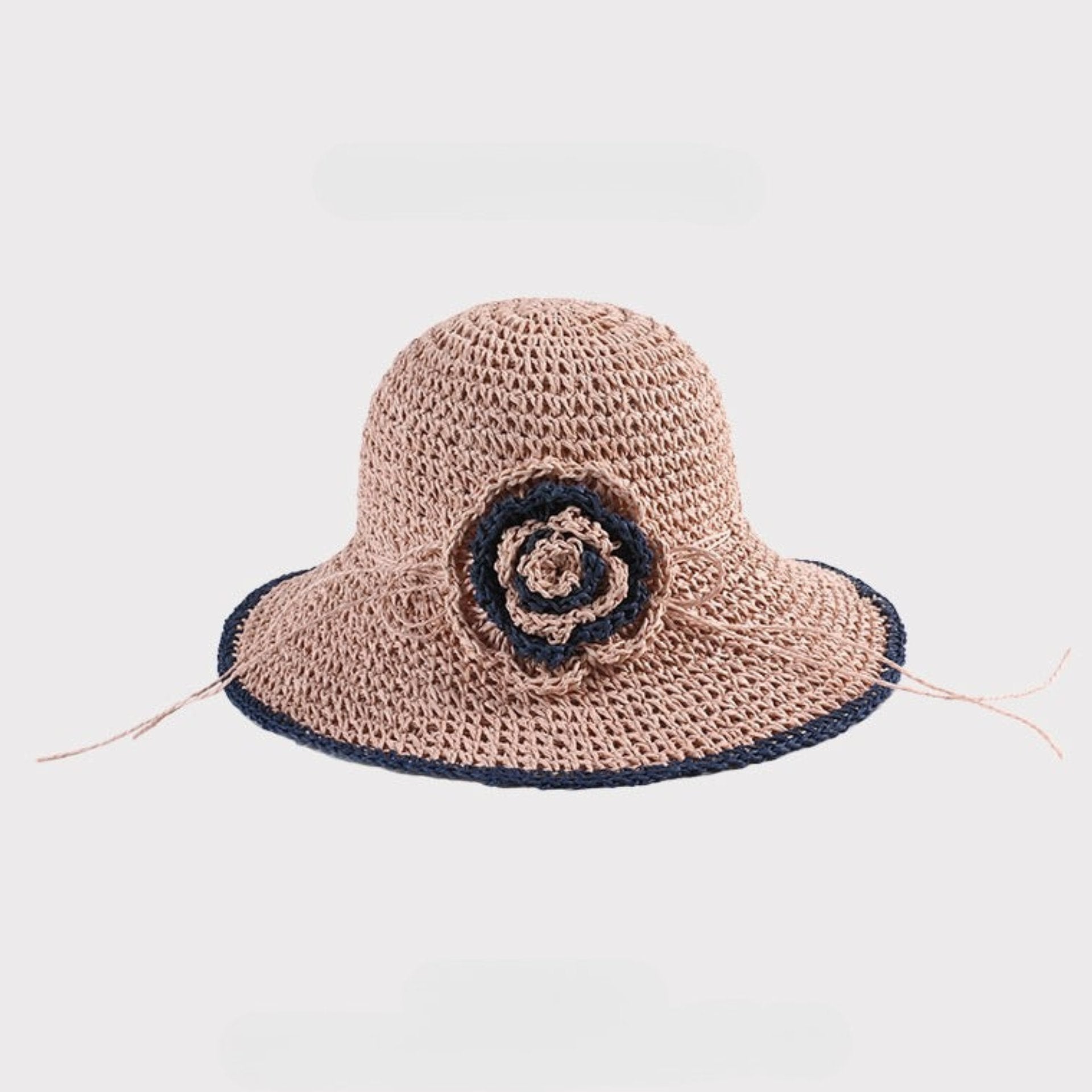  A pink woven sun hat with a navy crochet flower detail, featuring a flexible brim and an intricate woven texture.