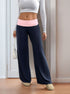 Front angle of navy blue wide-leg pants with a pink waistband, paired with a white long-sleeve top and beige slippers, model holding a white handbag.