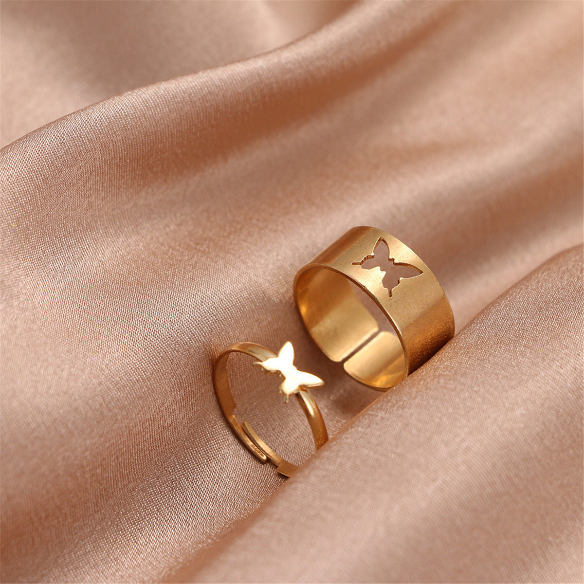 Gold butterfly rings on champagne silk: wide band with cutout and delicate band with raised butterfly