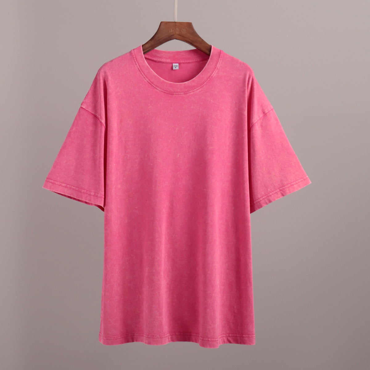Pink t-shirt on a wooden hanger against a gray background