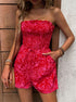 Woman in a red smocked romper with a drawstring waist, posing against a wooden door.