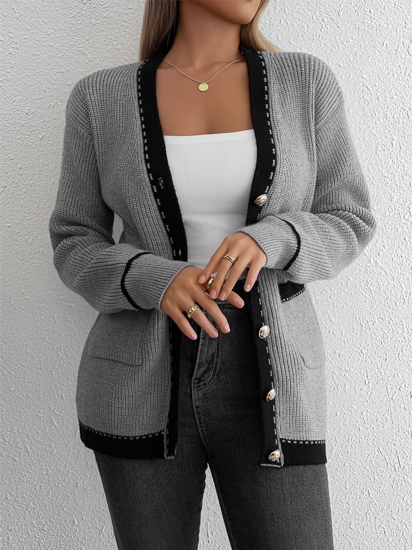 Close-up of gray knit cardigan with black trim and gold buttons, showing side pockets and detailed stitching