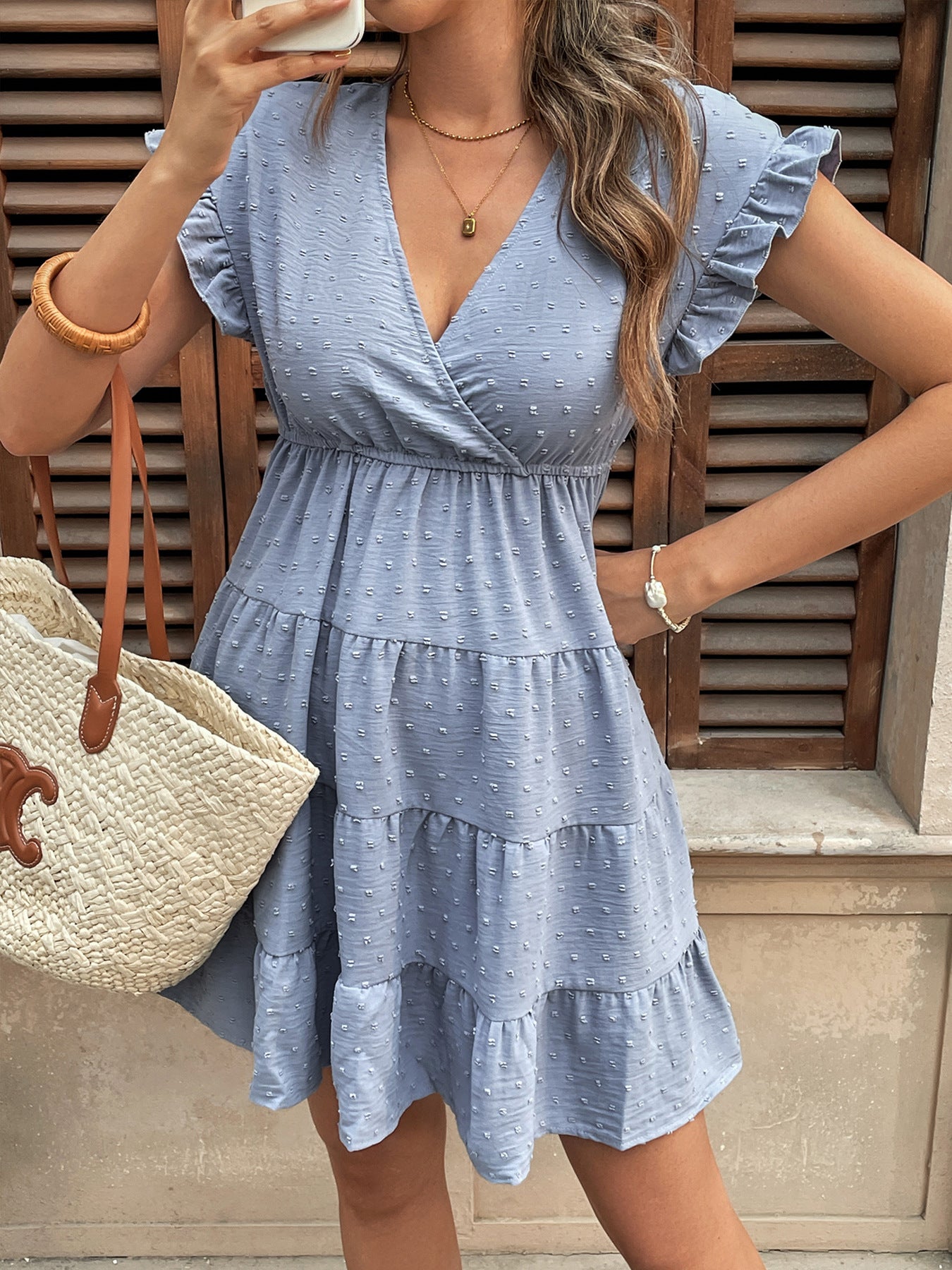 Woman taking a mirror selfie wearing a baby blue ruffle sleeve babydoll dress with a woven tote.