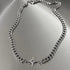 Full view of silver Cuban chain necklace laid flat on metallic surface, featuring eight-pointed star pendant with crystal accent