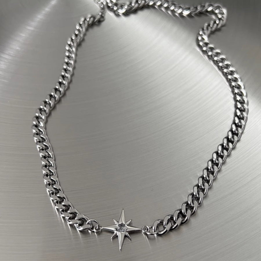 Full view of silver Cuban chain necklace laid flat on metallic surface, featuring eight-pointed star pendant with crystal accent