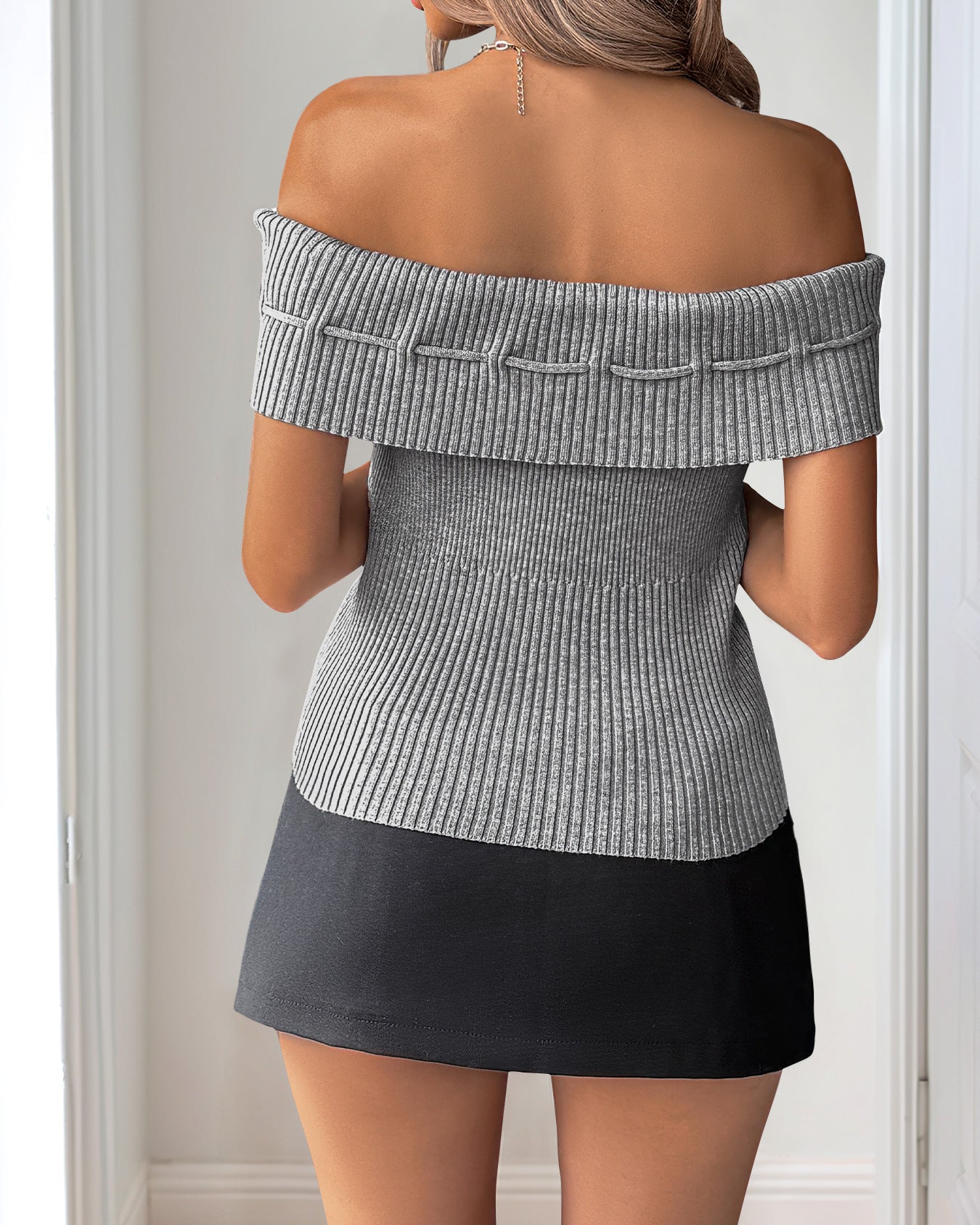 Back view of a woman in a gray off-shoulder ribbed top with fold-over detailing, styled with a black mini skirt.
