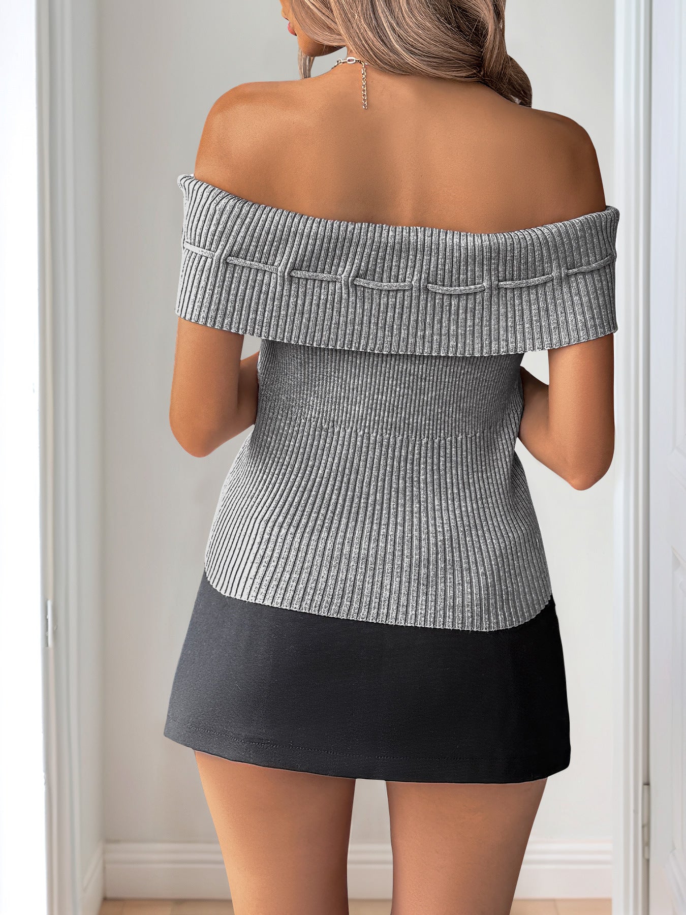 Back view of a woman in a gray off-shoulder ribbed top with fold-over detailing, styled with a black mini skirt.