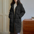 Black long puffer coat with flap pockets and high neck, worn with cream turtleneck against paneled wall