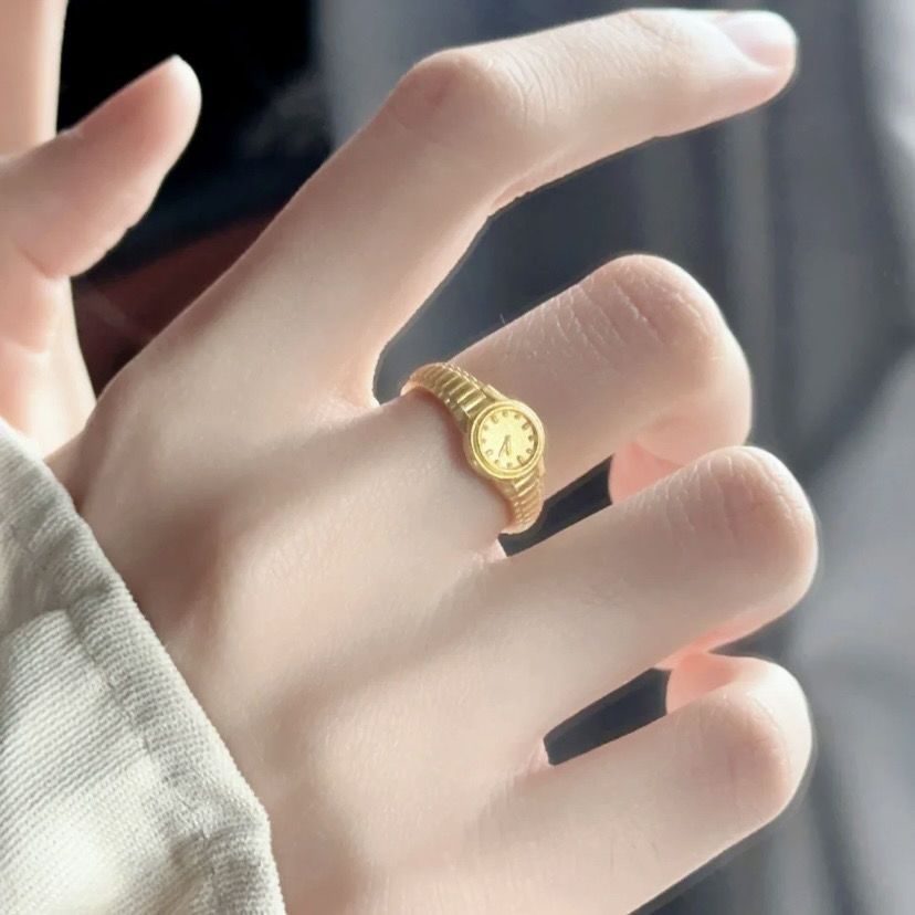 A gold mini-watch ring with expandable band design worn on finger, showcasing tiny functional timepiece display