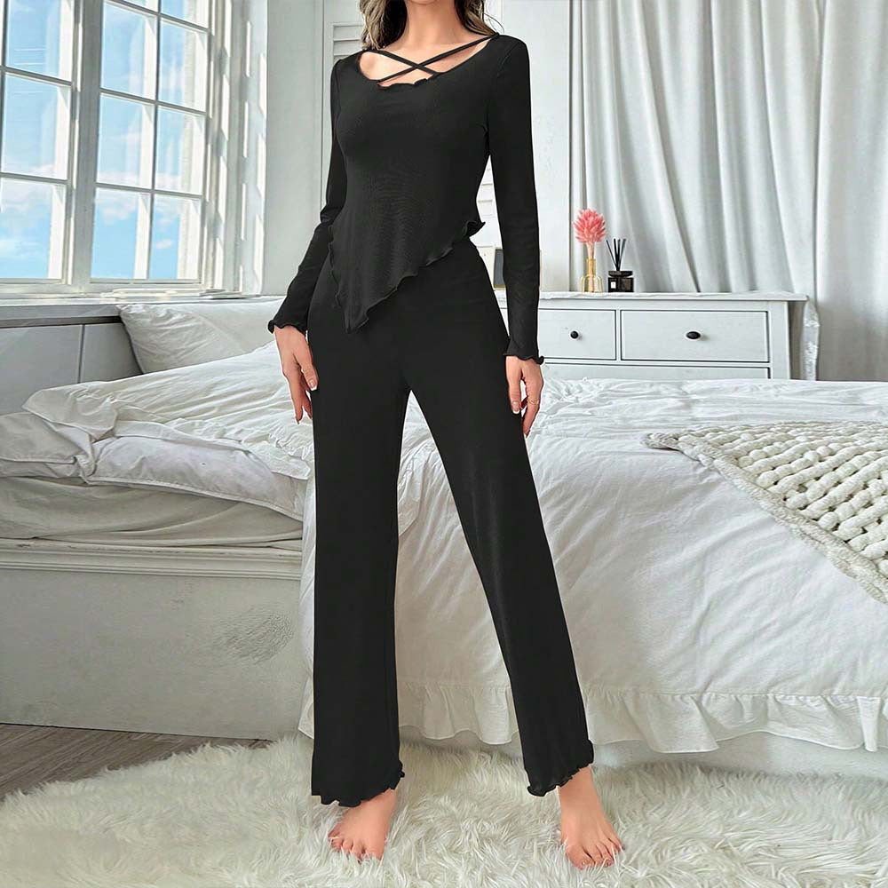 Front view of black stretch loungewear jumpsuit with diagonal ruffle detail and wide-leg pants, styled in modern bedroom setting