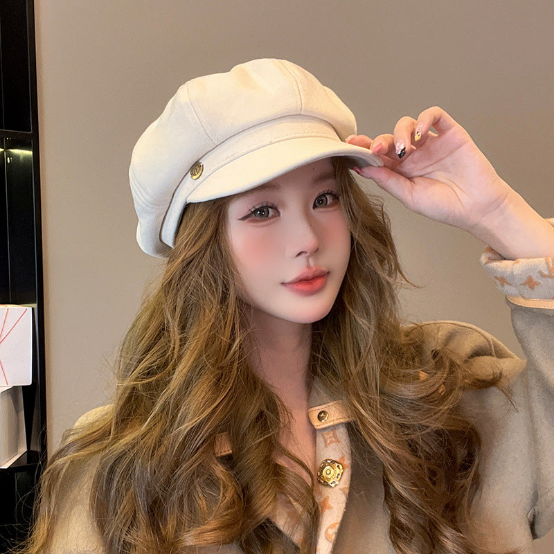 Woman touching brim of white newsboy cap with long wavy hair and designer pattern collar visible