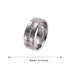 A close-up of a wide-band stainless steel ring with sparkling embedded stones, set on a textured black backdrop.