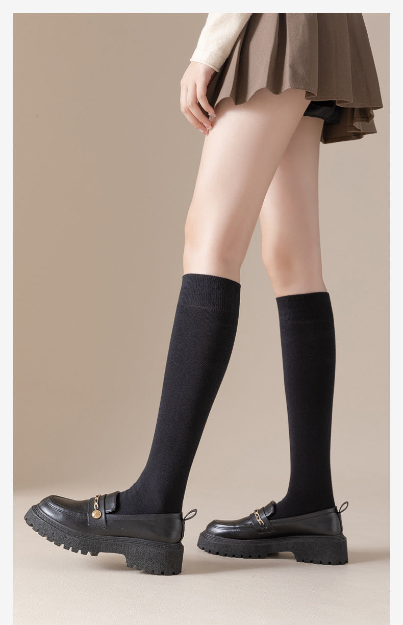 Person wearing beige skirt, cream sweater and black knee-high socks with platform loafers