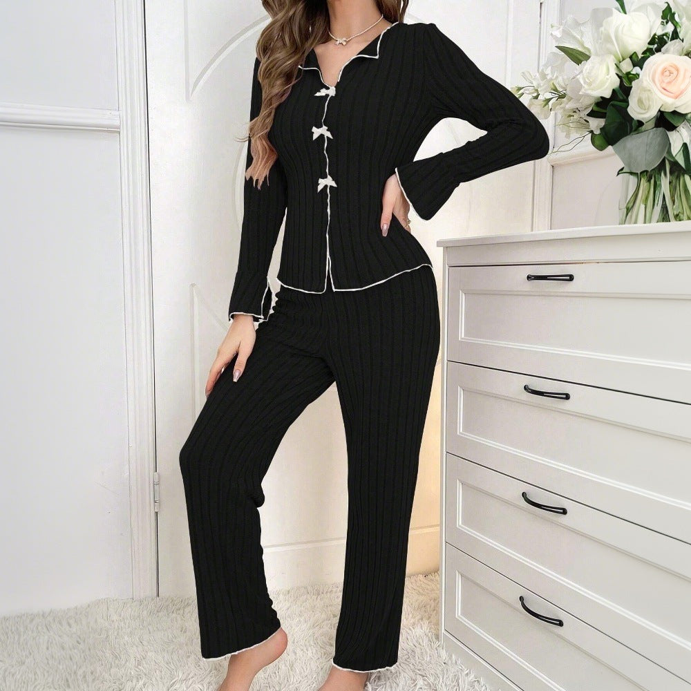 Full-length view of black ribbed pajama set with white piping and bow details, styled in bright white room with floral accents