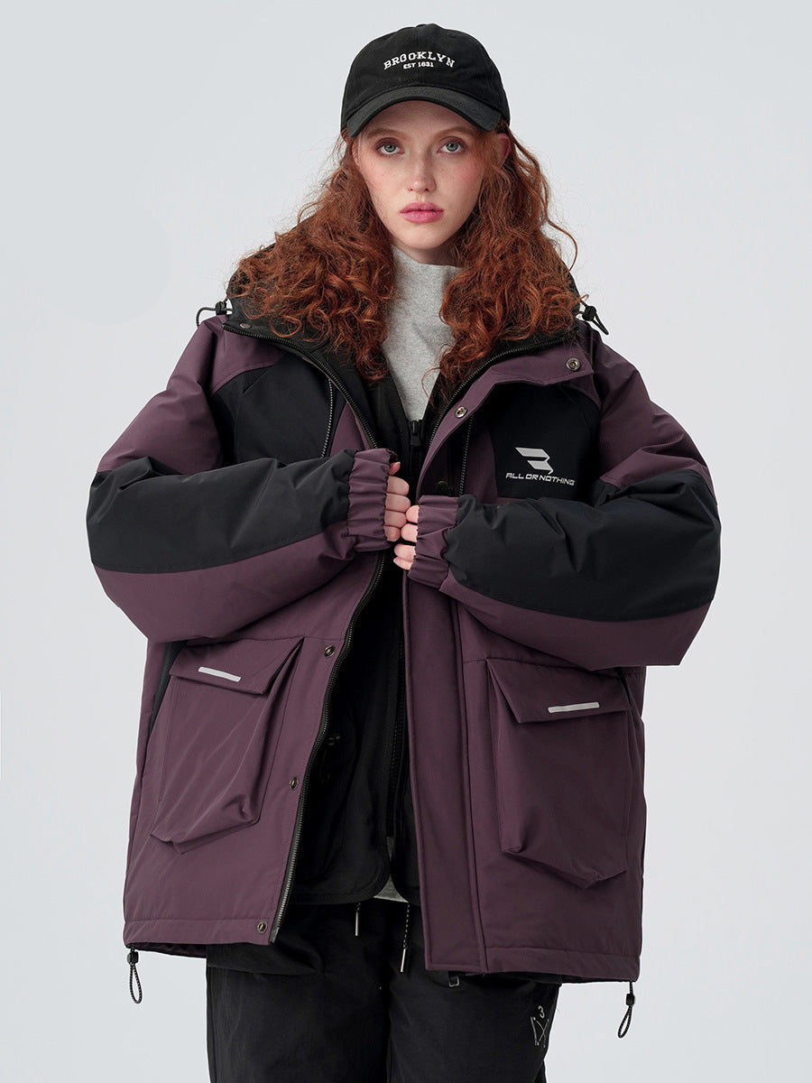 A woman with curly red hair wearing a Brooklyn cap clasps hands over her plum and black All Drifting jacket against white background