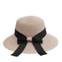 Close-up of a beige straw sun hat with a wide brim, featuring a black ribbon bow tied at the back.