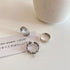 Three silver rings arranged on cream surface with a note reading 'the dream (2020)' - Roman numeral, layered band, and chain designs