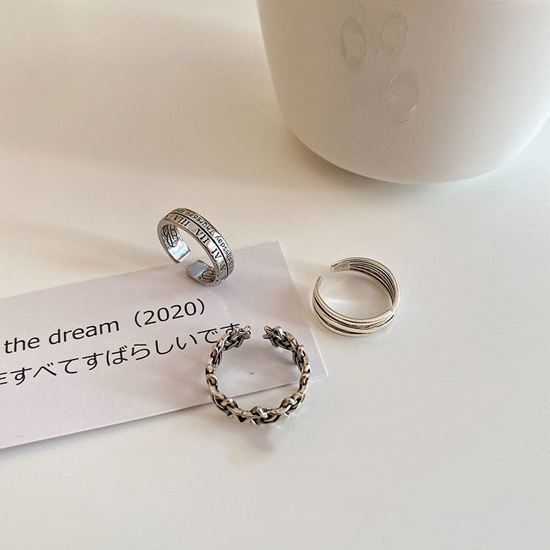 Three silver rings arranged on cream surface with a note reading 'the dream (2020)' - Roman numeral, layered band, and chain designs