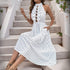 Model sitting on steps, wearing a white polka dot ruffled halter dress with cutouts, holding the skirt for a flowy effect.
