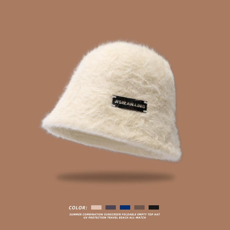 White fluffy bucket hat with a black logo patch, displayed against a brown background