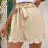 A model wearing cream scalloped hem shorts with elasticated paperbag waist and bow tie detail against wall background